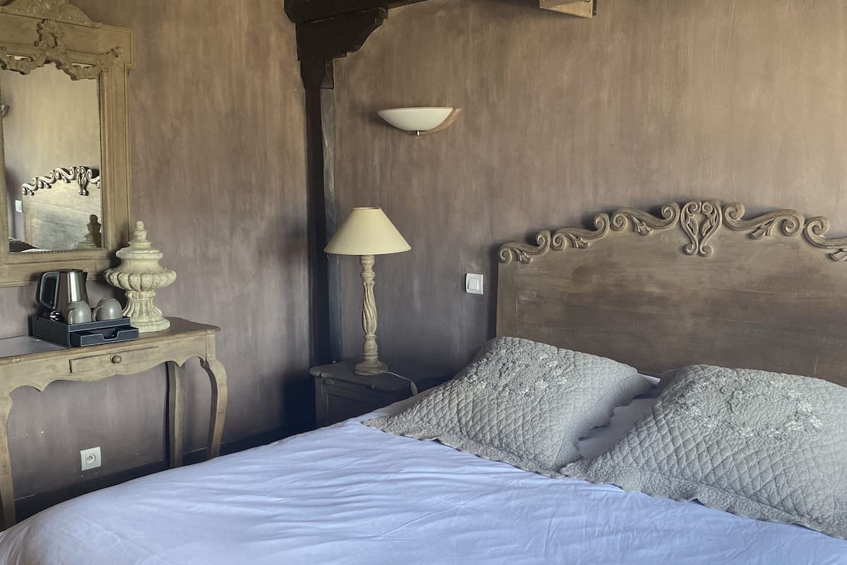 A bedroom with a large bed, a nightstand with a lamp, a dresser with a mirror, and a decorative wall panel.