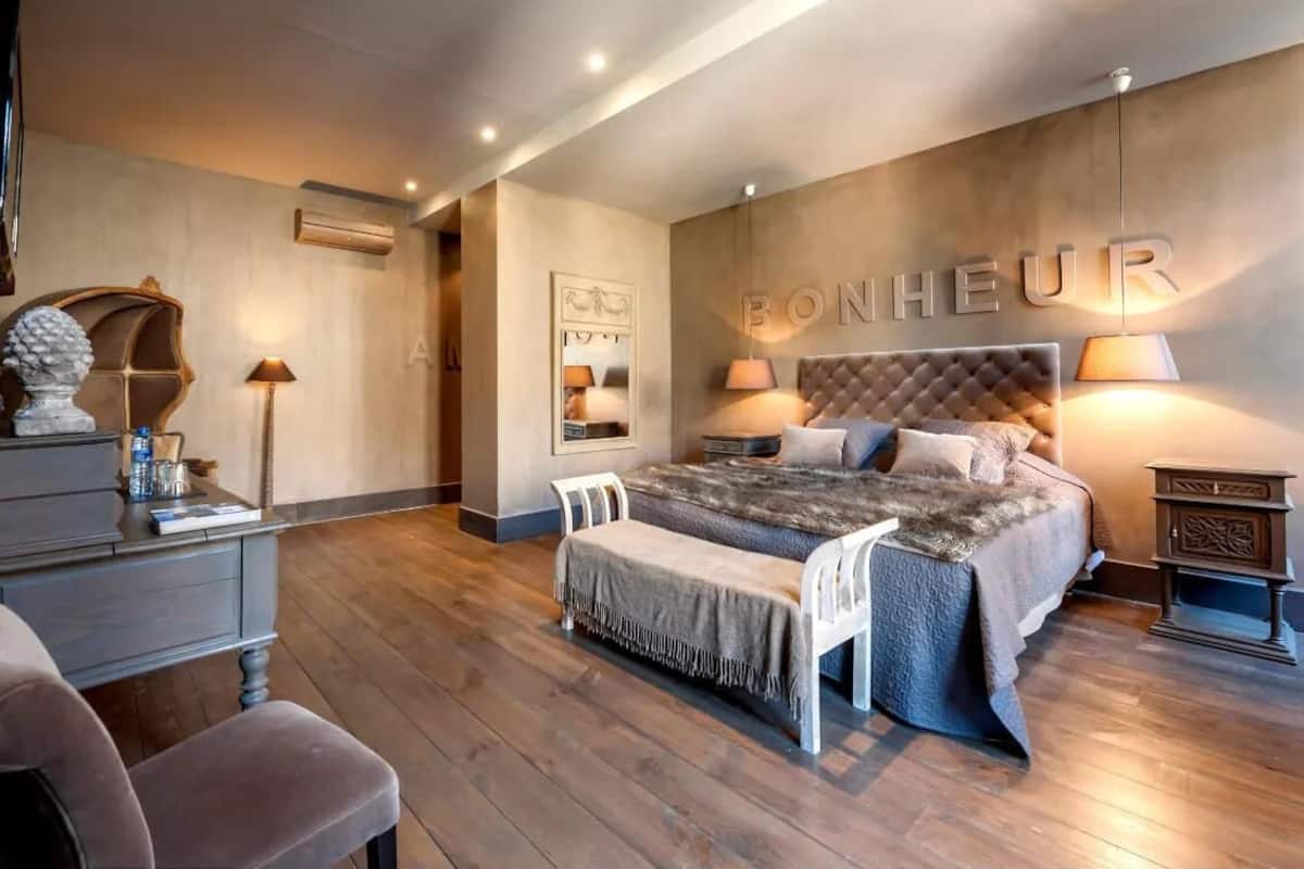A bedroom with a large bed, bedside tables, a chair, and a wall-mounted sign that reads "BONHEUR".