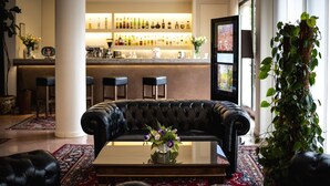 Una zona de bar con mostrador y taburetes, un sofá de cuero con un florero y una planta grande en maceta.