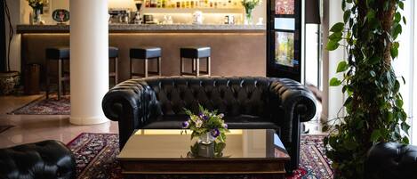 Un espace bar avec un comptoir et des tabourets, un canapé en cuir agrémenté d’un vase de fleurs et une grande plante en pot.