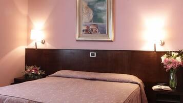 A hotel room with a large bed, two bedside lamps, a painting on the wall, and a vase with flowers on the nightstand.
