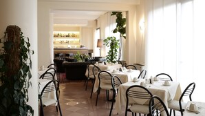 Un comedor con mesas dispuestas para el servicio, una barra al fondo y una planta grande en el centro.