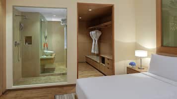 A hotel room with a walk-in closet, a separate bathroom with a glass shower enclosure, and a bedside table with a lamp.