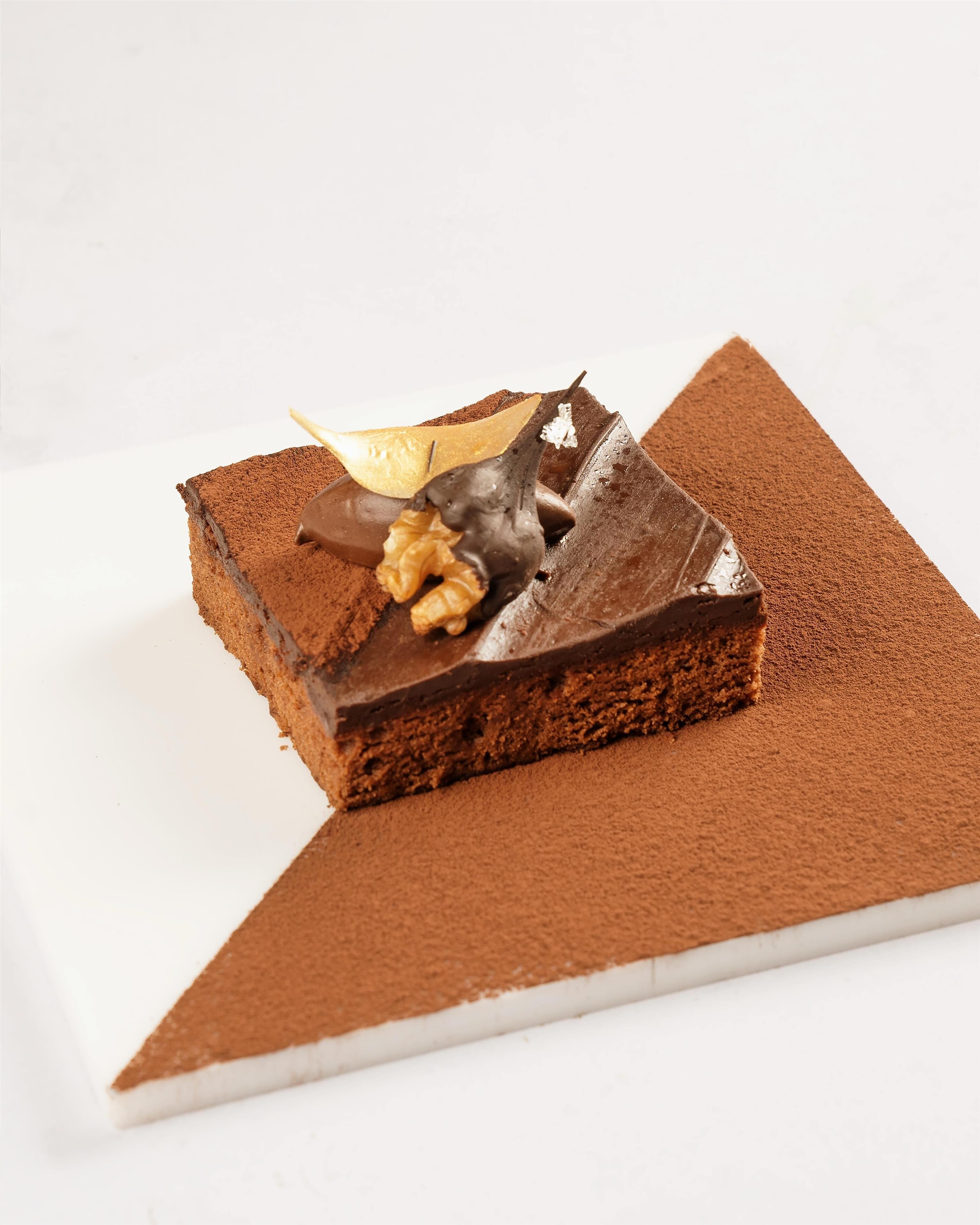 A slice of chocolate cake with a decorative chocolate piece and a walnut on a white plate.