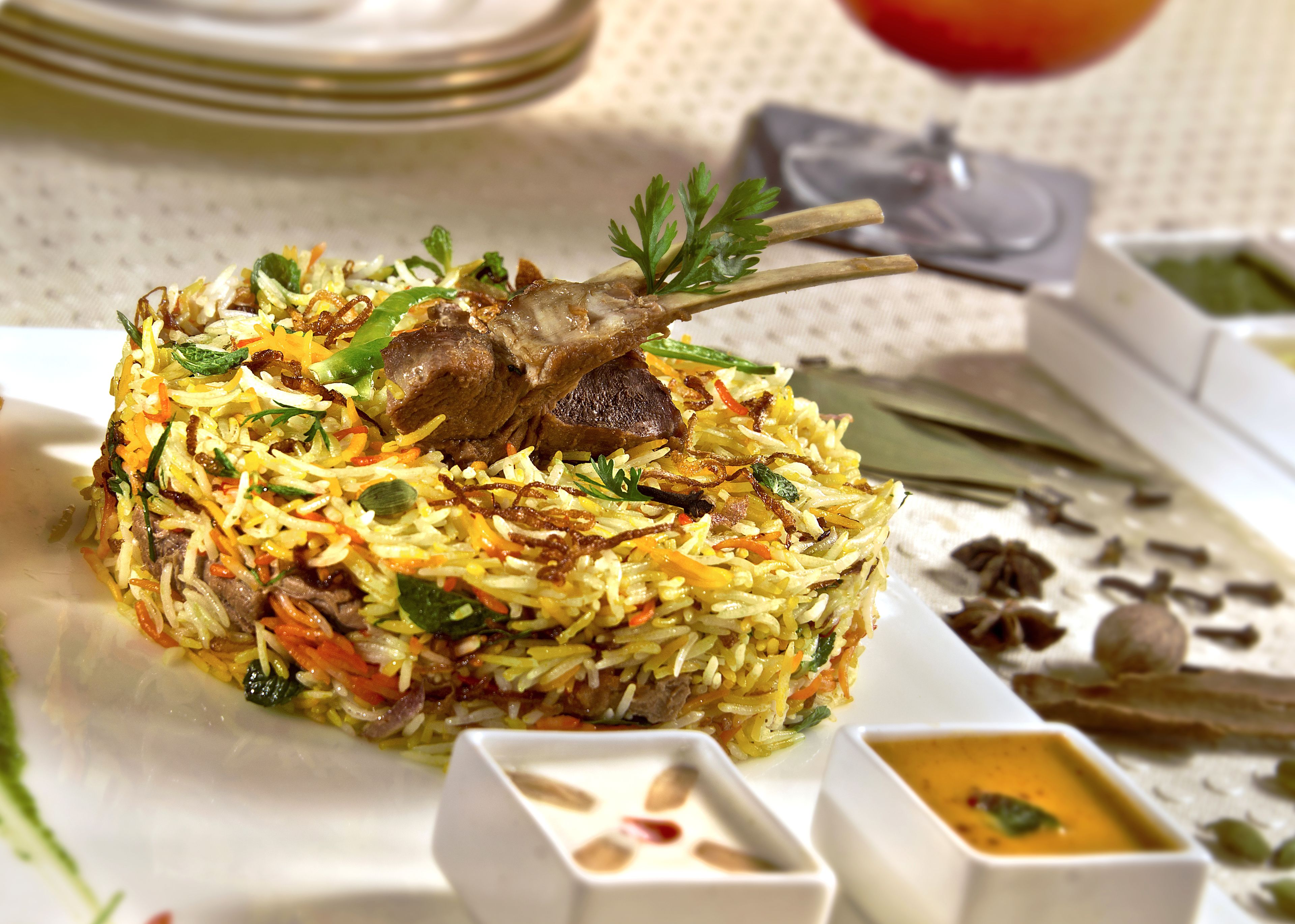 Une assiette de biryani, un plat de riz aux épices, garni de viande et de légumes, accompagné de deux petits bols de sauce.