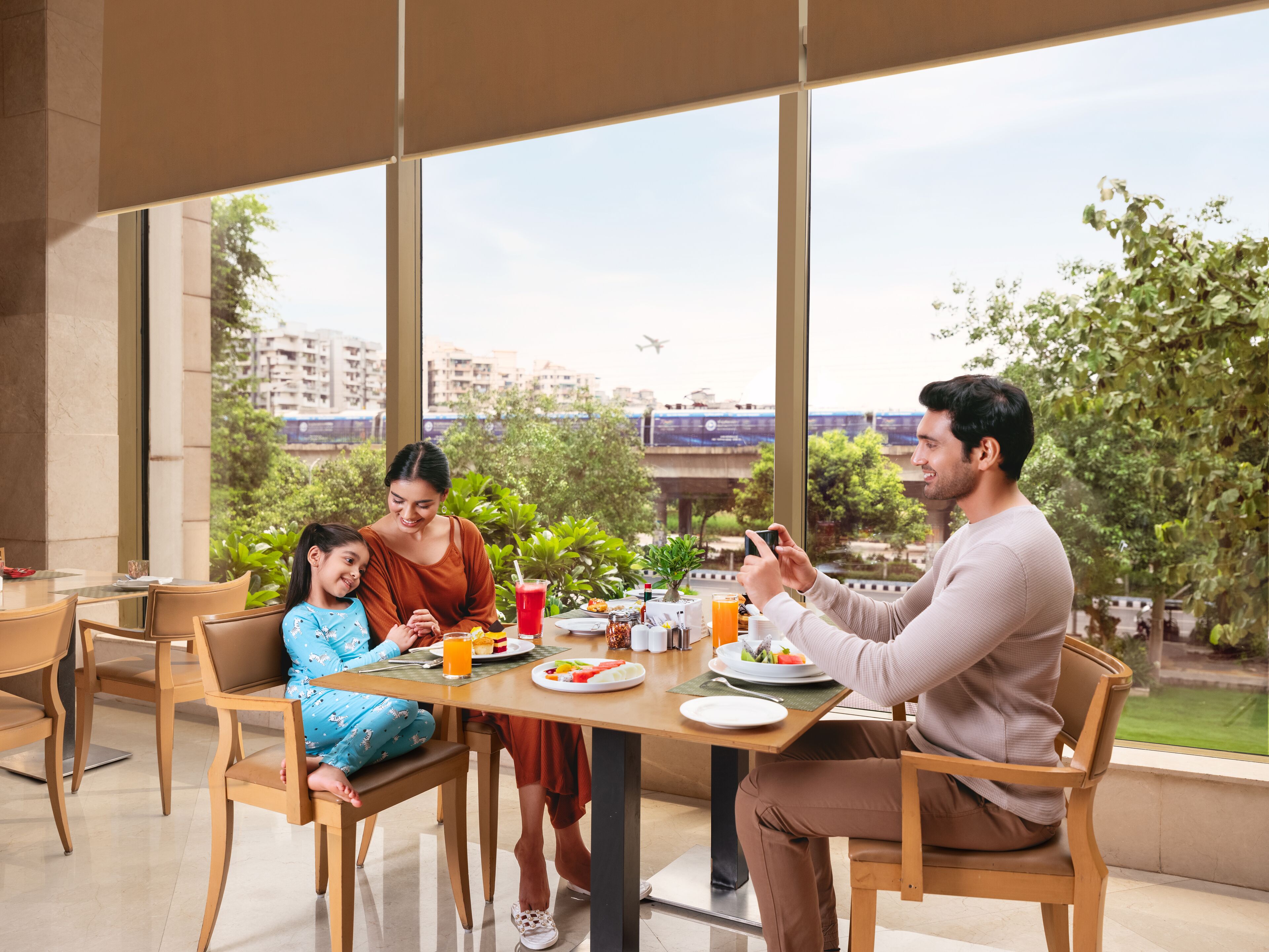 A family dining at a table with a city view, including a train and greenery.