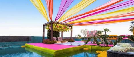 A pool area with a stage and seating, surrounded by colorful drapes and floral arrangements.
