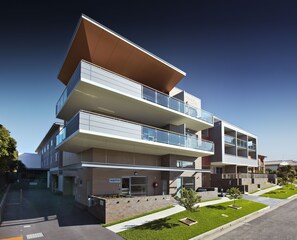 A modern multi-story building with a reception area, glass balconies, and a well-maintained lawn. - Charlestown Executive Apartments (Charlestown)