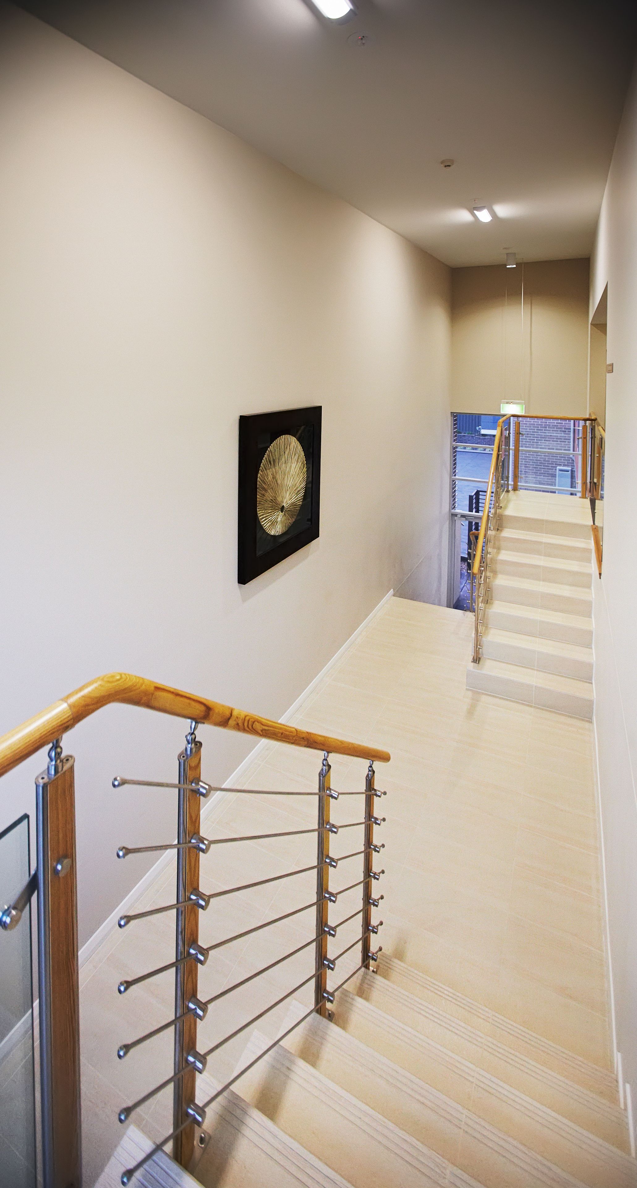 Eine Treppe mit hölzernen Geländern und Metallspindeln, die zu einer Zwischenebene mit einem gerahmten Kunstwerk führt.