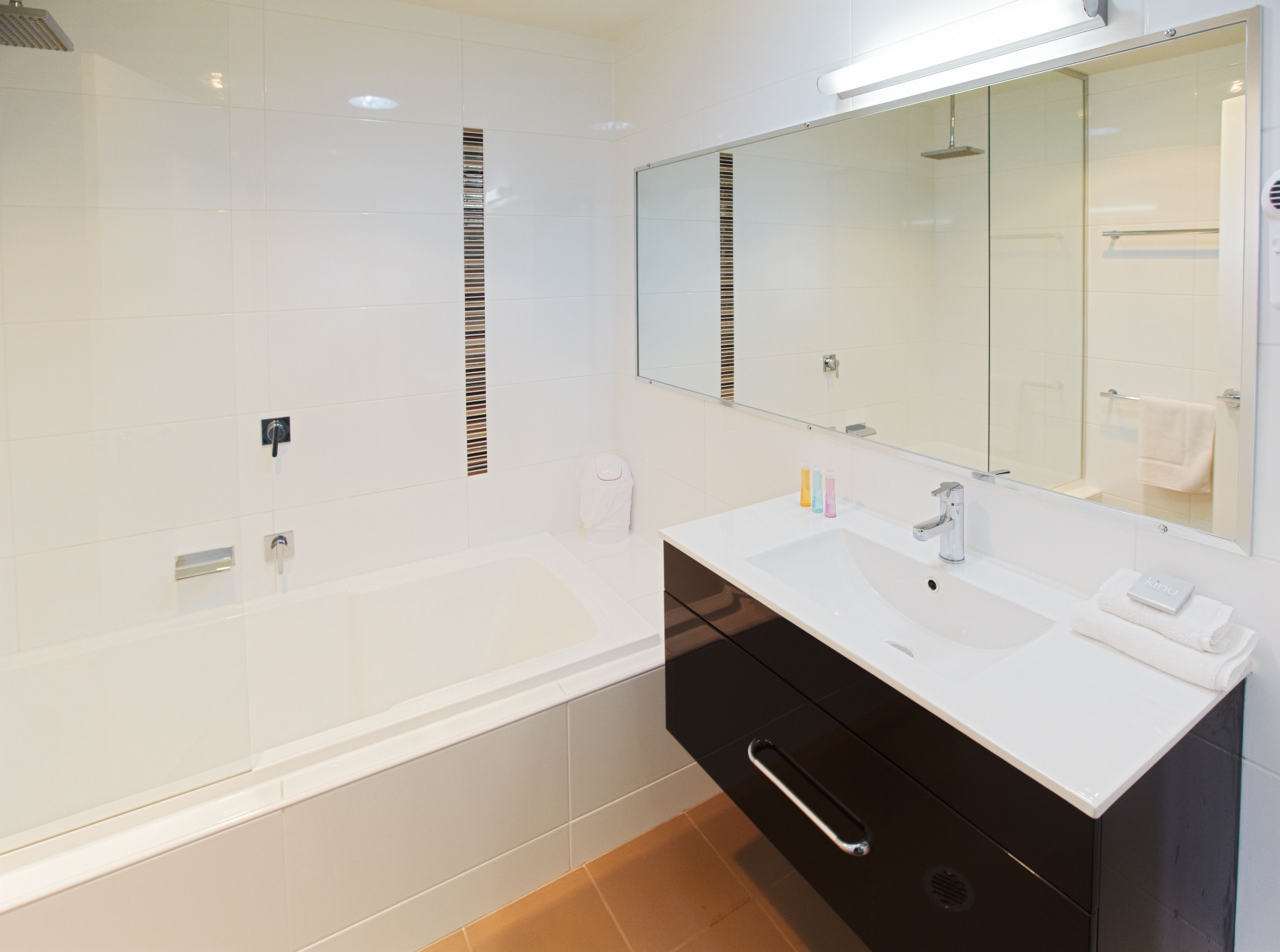 Een moderne badkamer met een wit wastafel, een zwart kastje en een grote spiegel.