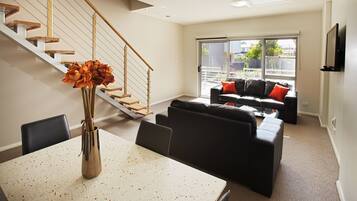 A modern living room with a staircase, a dining area with a table and chairs, and a sofa set.