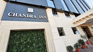 Exterior del Chandra Inn, con una fachada moderna, un cartel llamativo, una entrada con muro verde y plantas en macetas.
