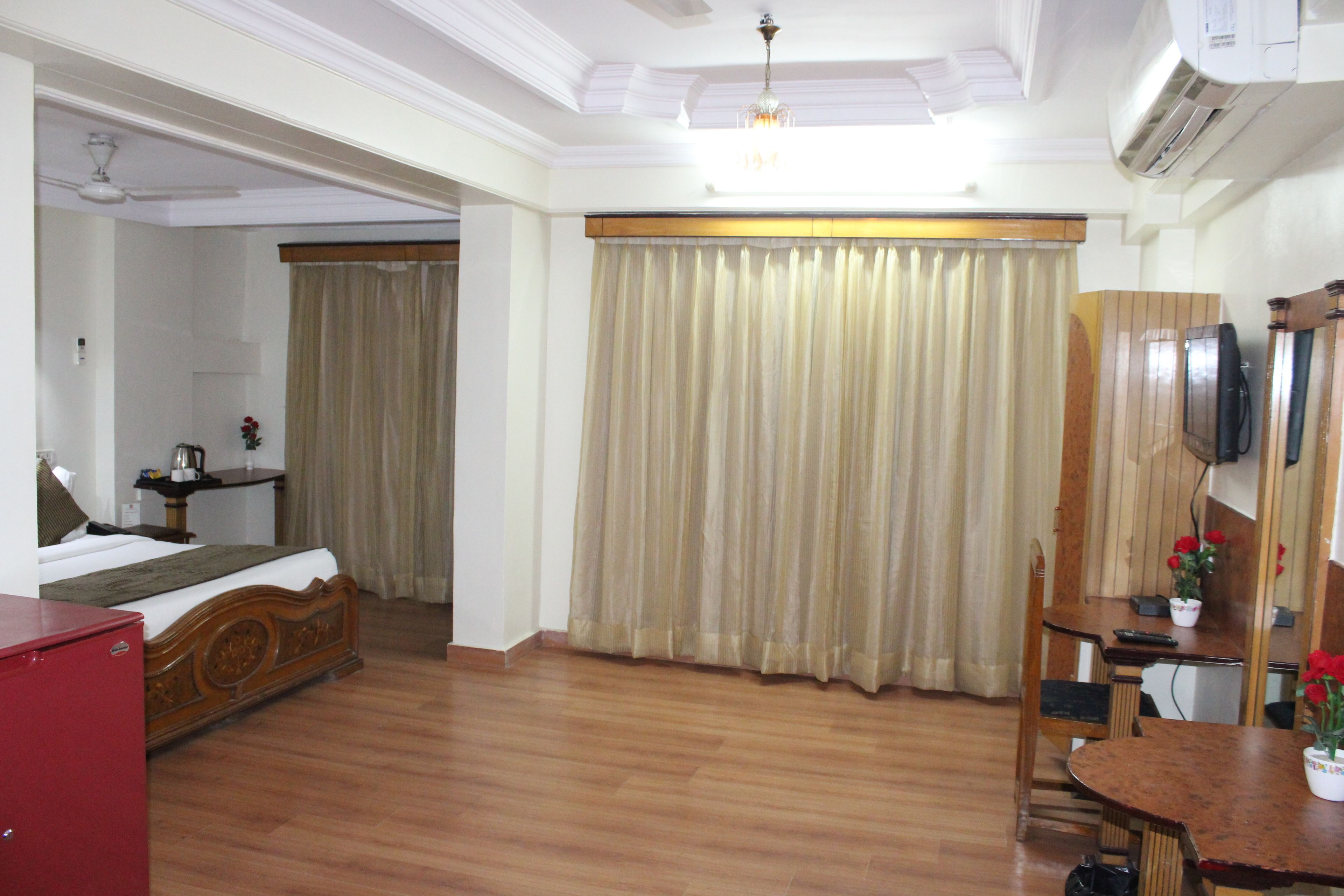 Habitación de hotel con piso de madera, una cama, un escritorio con silla, televisor y ventana con cortinas.