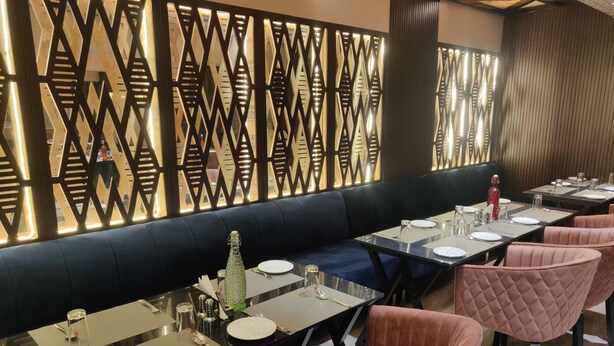 Un comedor con una mesa larga, asientos acolchados y una pared decorativa con motivos geométricos.