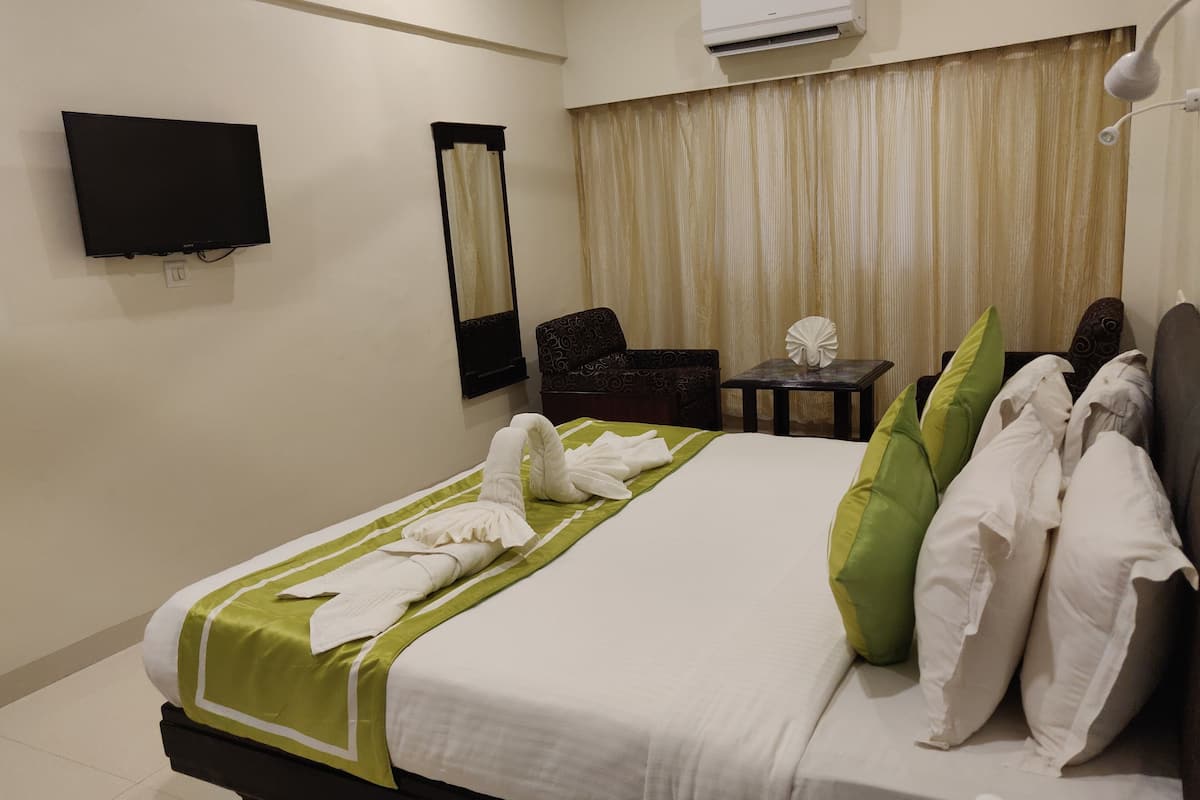 A hotel room with a neatly made bed, a flat-screen TV mounted on the wall, a small table with a decorative item, and a chair.
