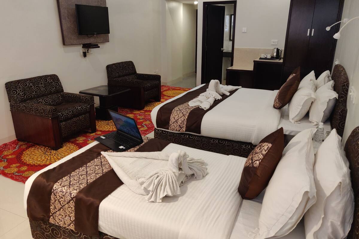 A hotel room with two beds, a desk, a chair, a TV, and a wardrobe.