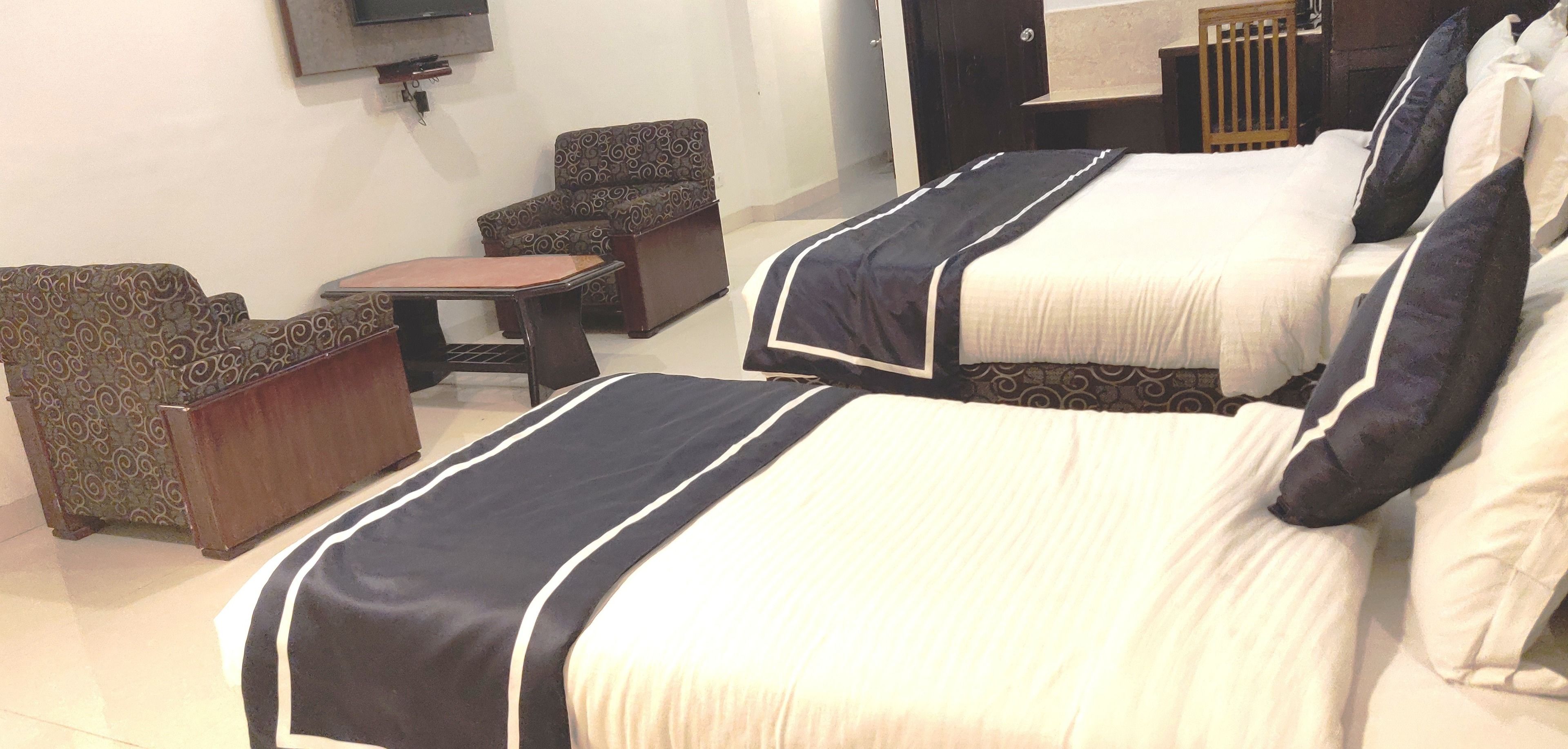 A hotel room with two beds, a sofa, a small table, and a TV mounted on the wall.