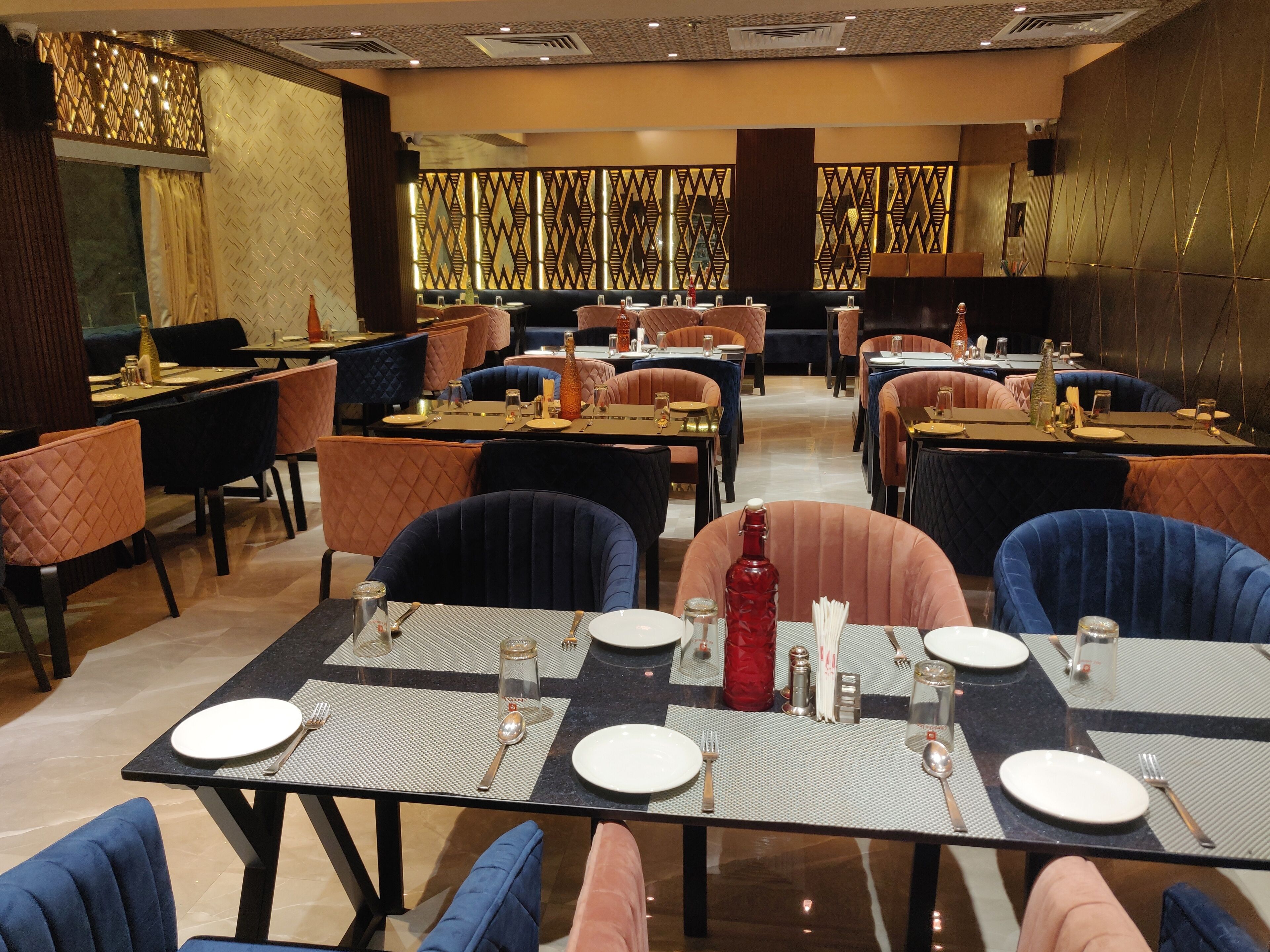 Un restaurant où les tables sont dressées pour le service, avec un design moderne, des murs décorés de motifs et des chaises rembourrées.