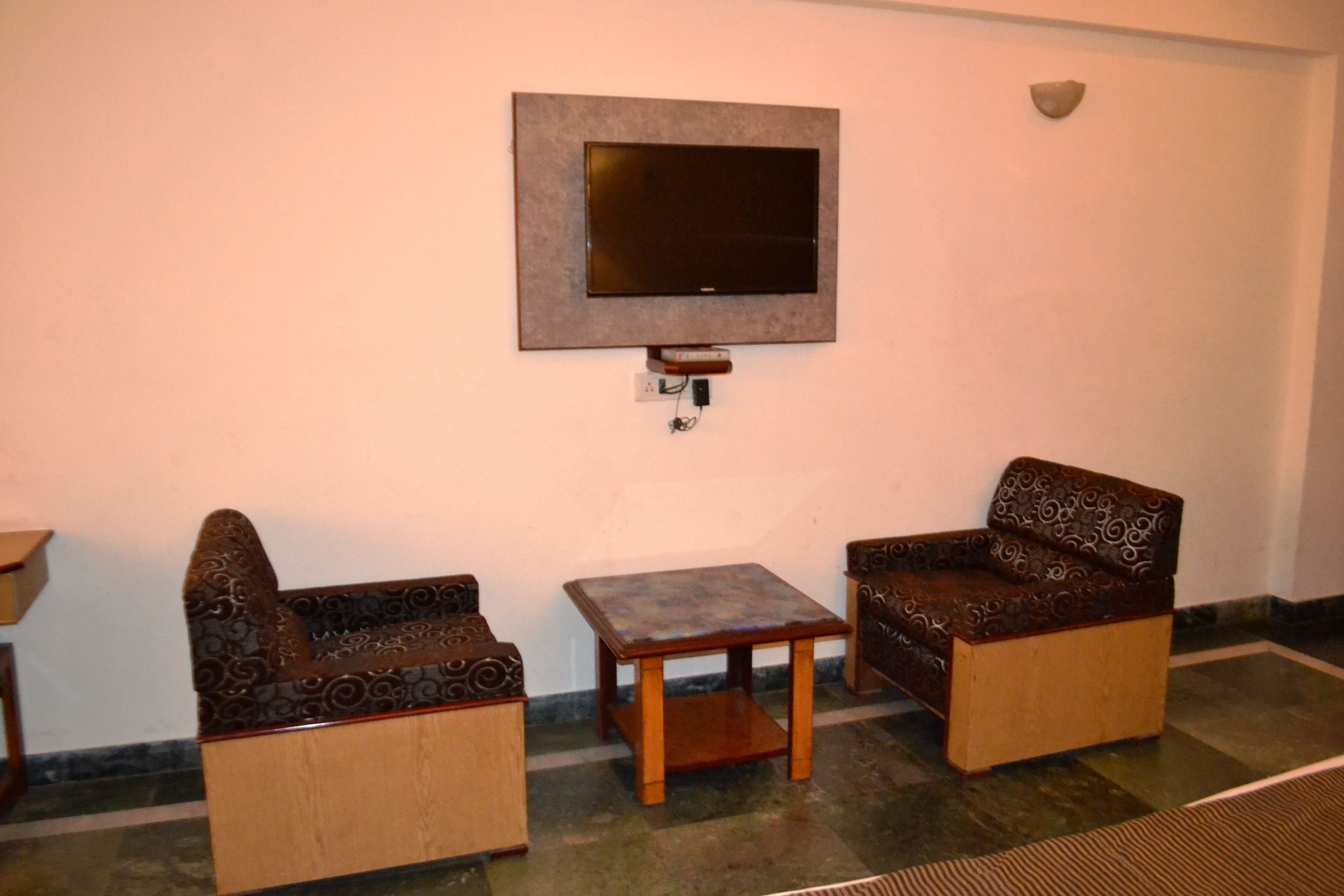 A room with a flat-screen TV mounted on the wall, two patterned armchairs, and a small wooden table.