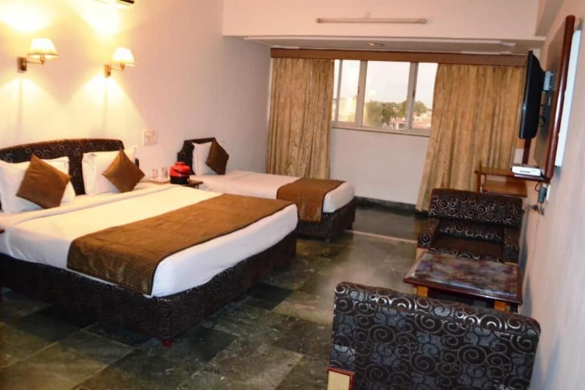 A hotel room with two beds, a television, a window with curtains, and a small table.