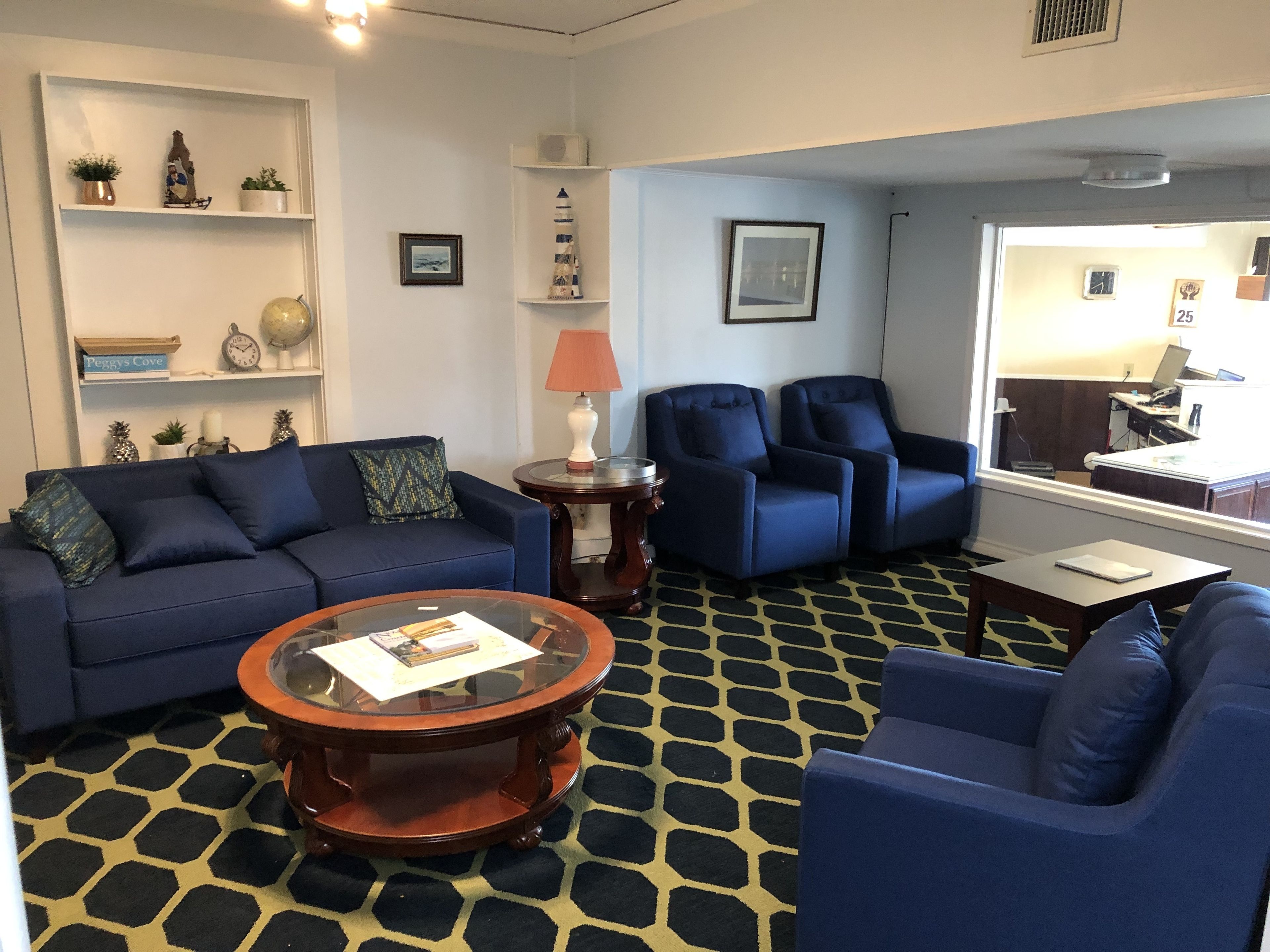 A living room with a blue sofa, two blue armchairs, a glass coffee table, and a patterned floor.