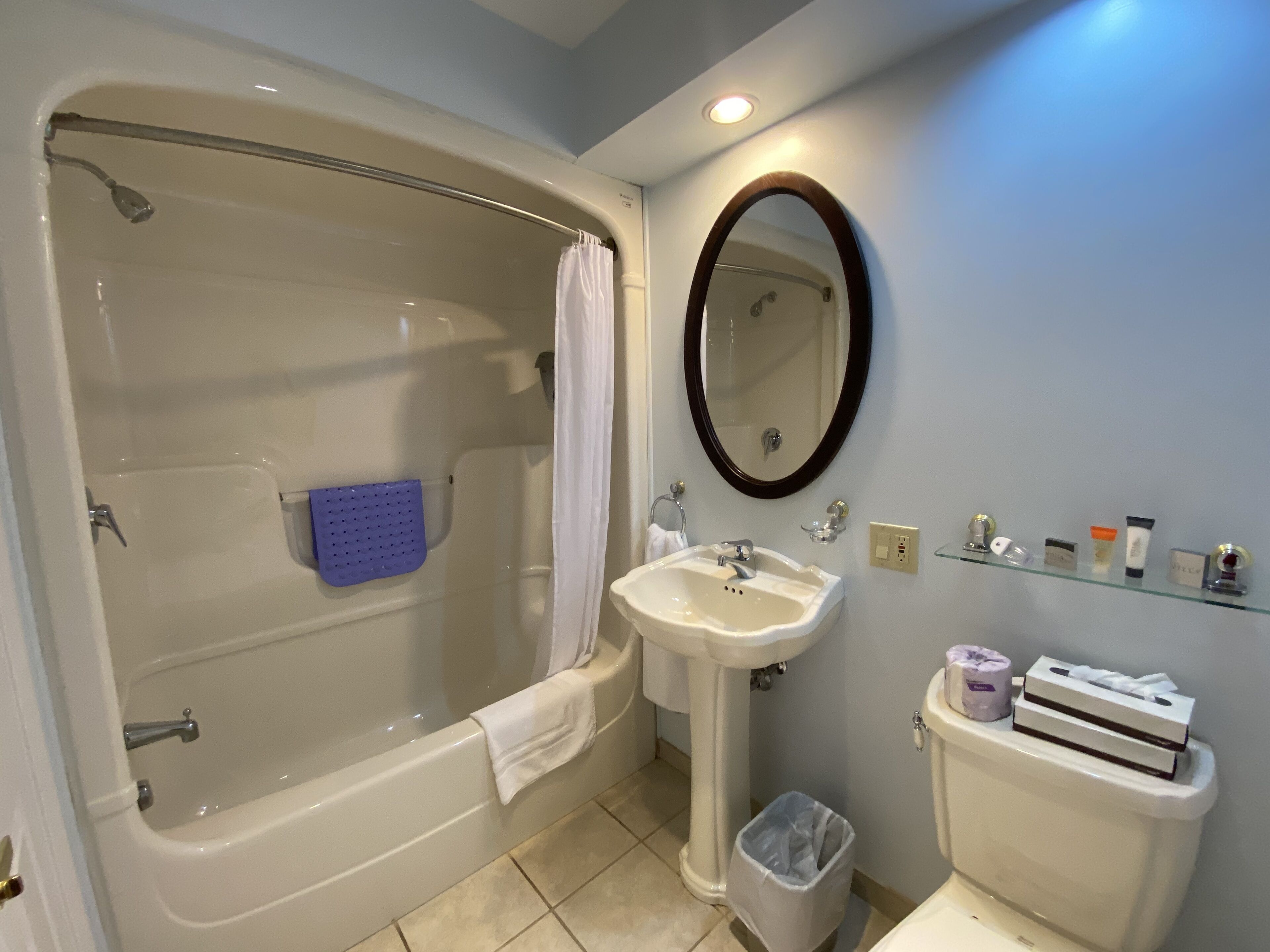 Une salle de bain avec une baignoire, un lavabo, un miroir et des articles de toilette fixés au mur.