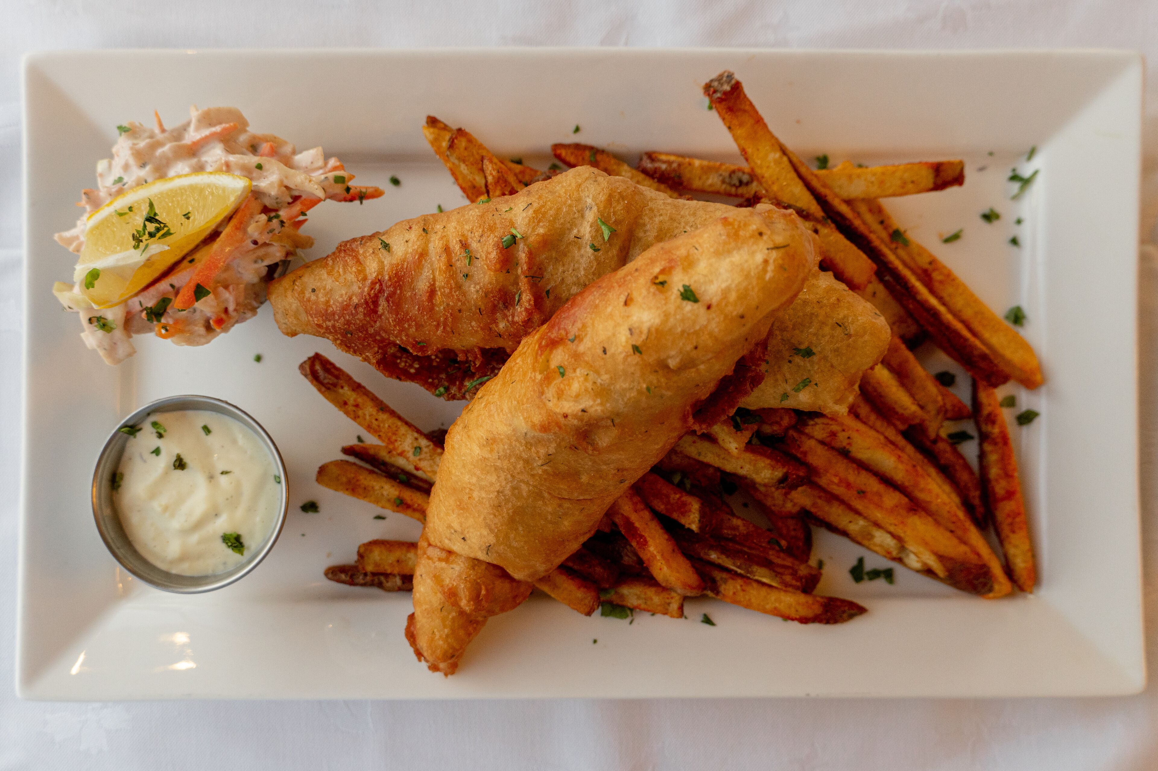 A plate of fish and chips with a side of tartar sauce and lemon.
