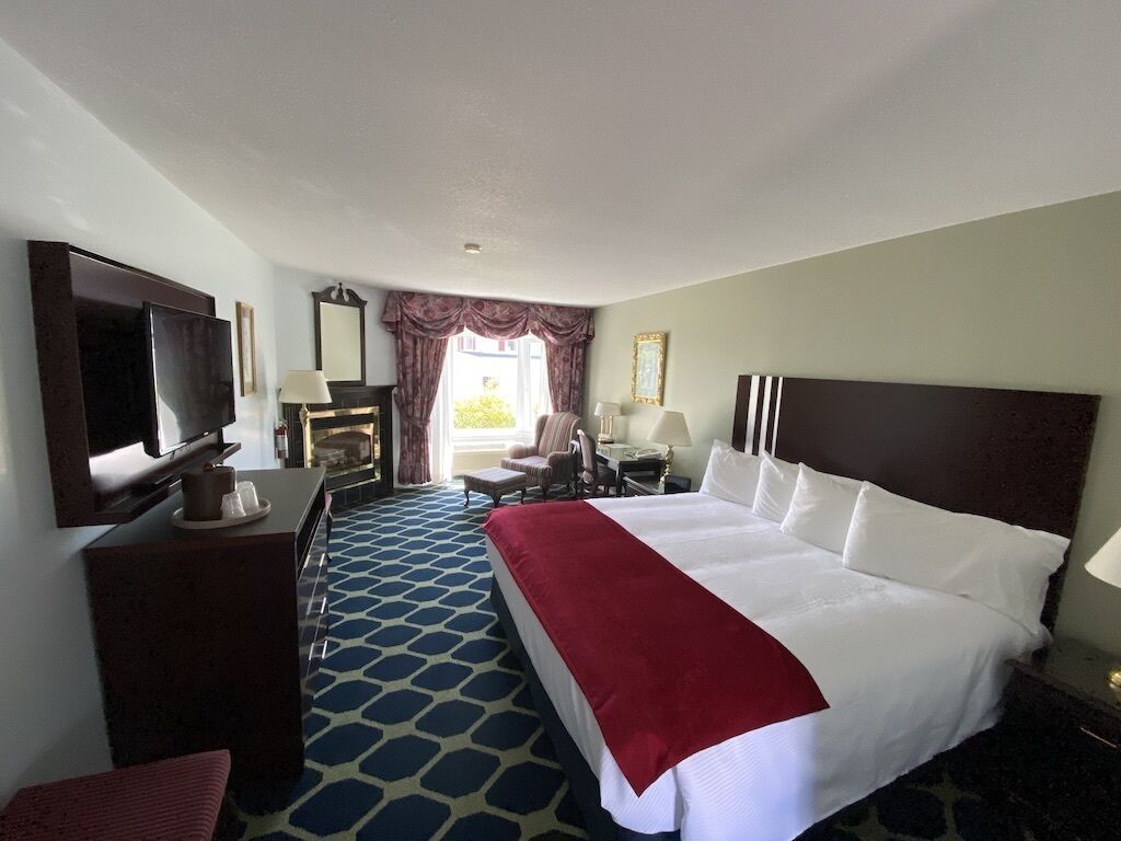 A hotel room with a large bed, a desk, a television, and a window with curtains.