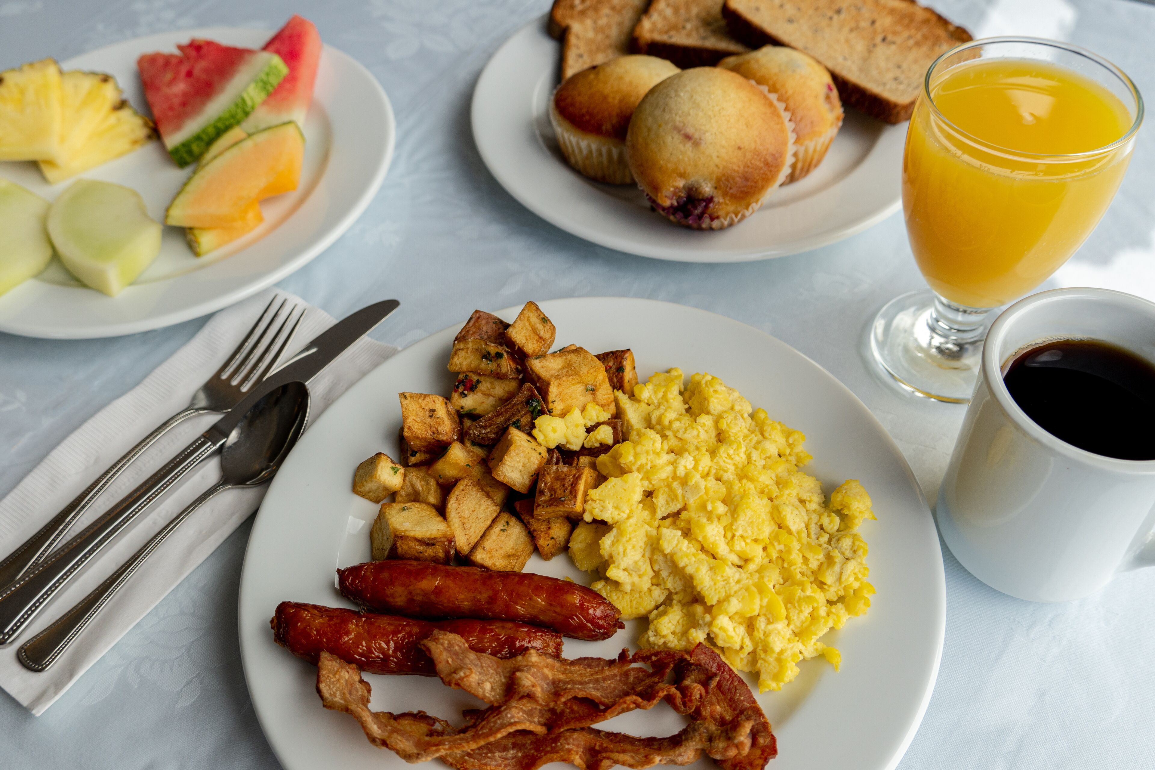A breakfast plate with scrambled eggs, bacon, sausage, hash browns, toast, and fruit.