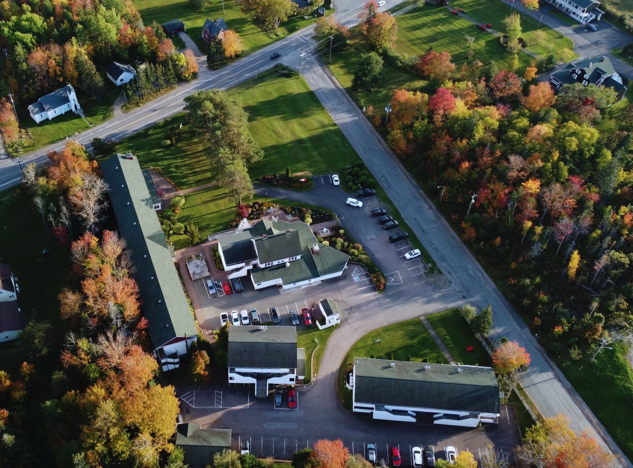 An aerial view of a commercial property with multiple buildings, parking lots, and surrounding trees.
