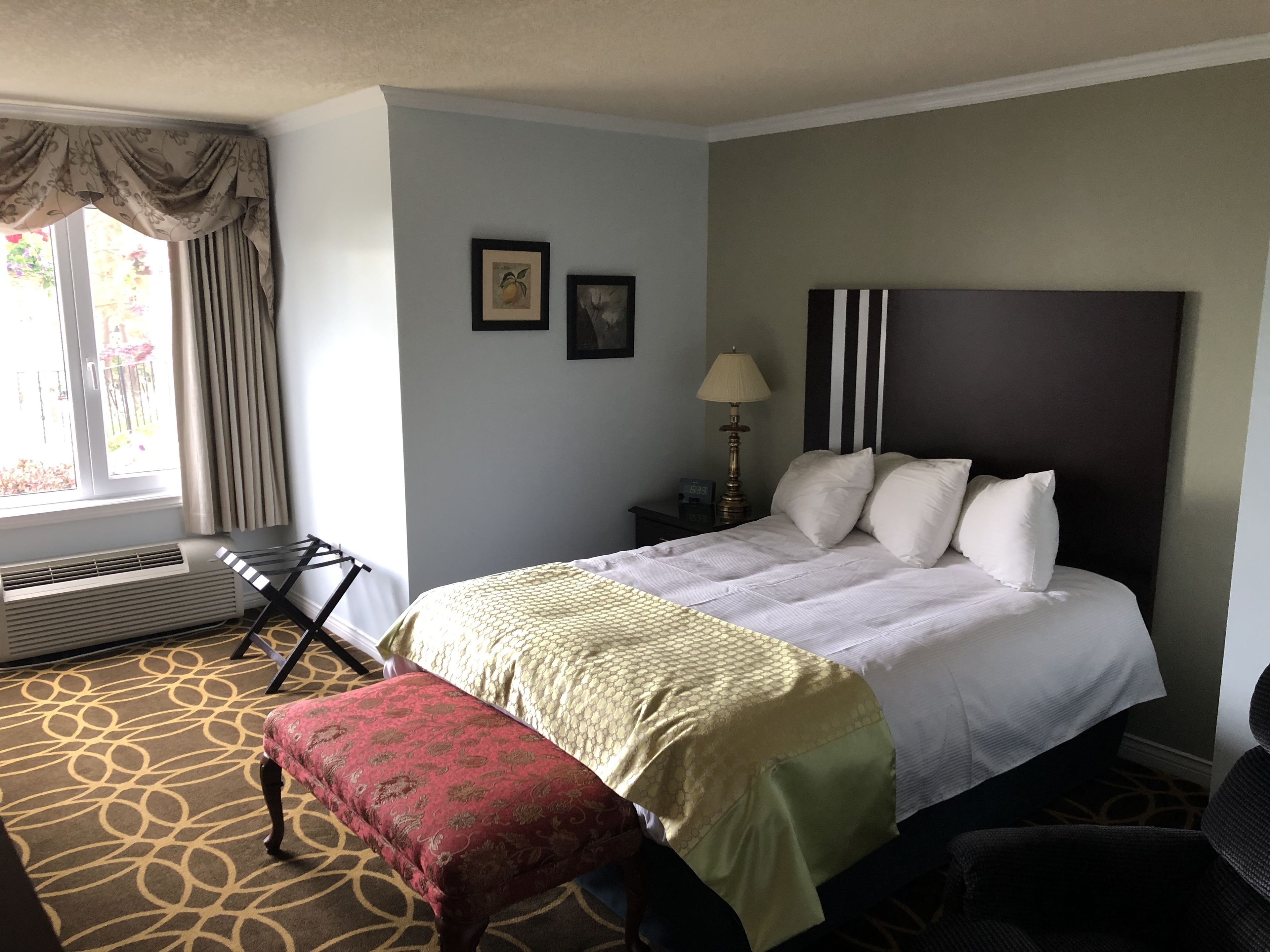A hotel room with a bed, a desk, a chair, a bench, and a window with curtains.
