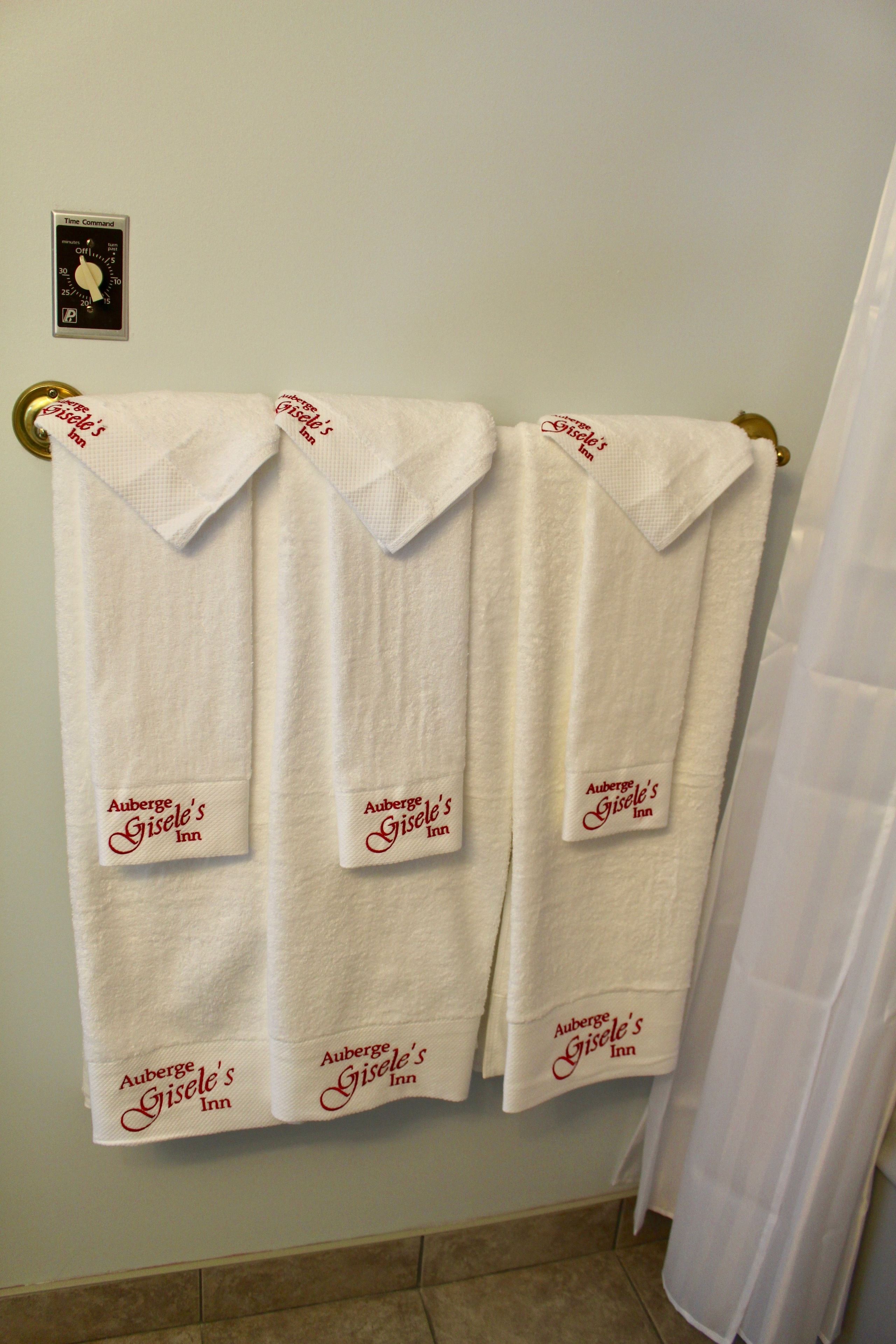 Three white towels hanging on a wall, each with the text "Auberge Gisèle's Inn" printed on them.