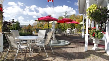 An outdoor patio with a round table and chairs, a flag, and potted plants.