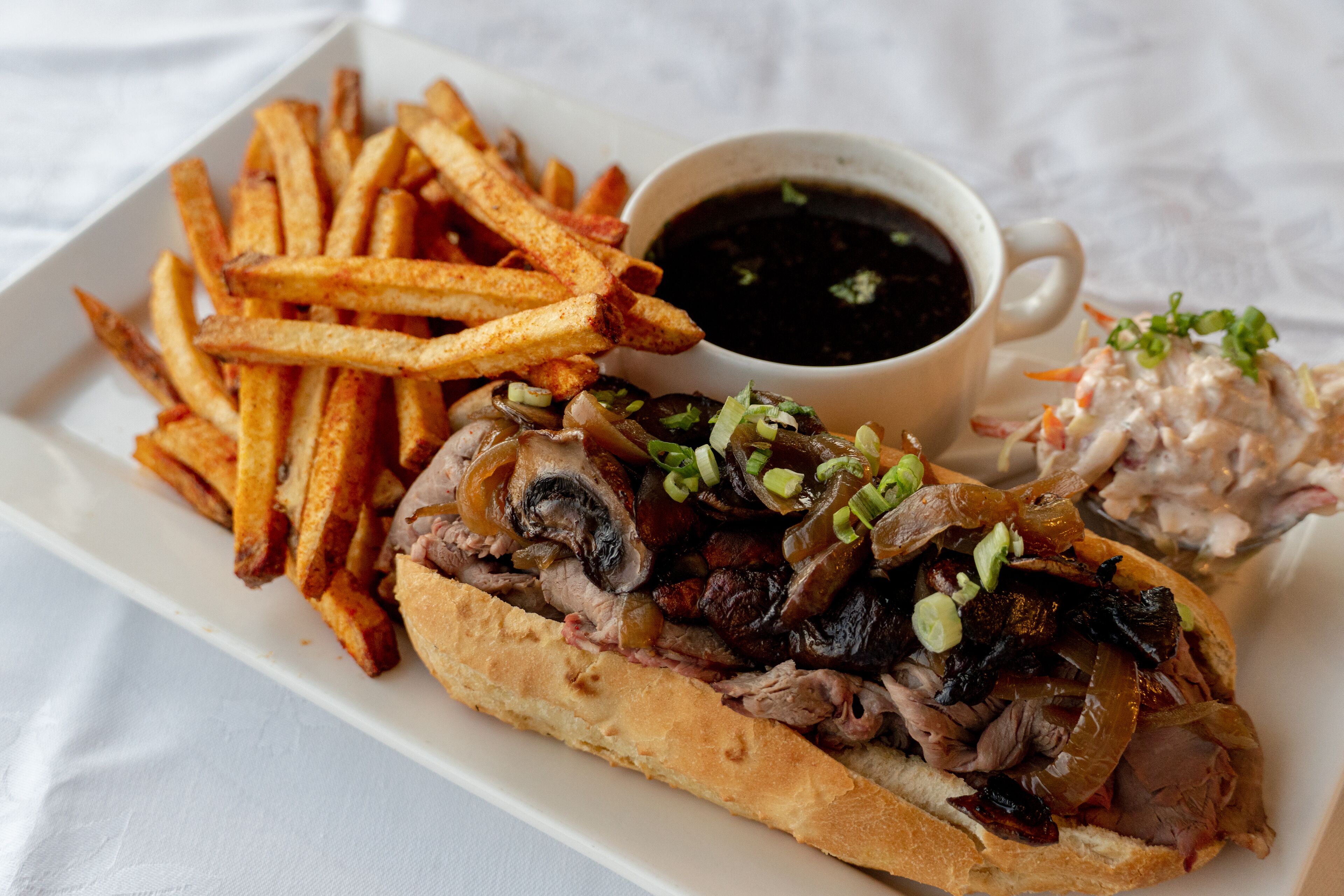 A plate of food including a sandwich, fries, and a cup of sauce.