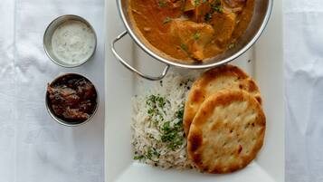 Un plato con arroz, pan naan y un plato de curry, acompañado de dos recipientes pequeños de chutney y raita.