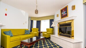 A living room with a yellow sofa, matching armchairs, a coffee table, a fireplace, and a patterned carpet. - Auberge Gisele's Inn (Baddeck)