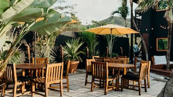 Une terrasse extérieure avec des tables et des chaises en bois, entourée de plantes en pot et de parasols.