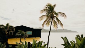 A modern building with a black facade and yellow awning, surrounded by tropical plants and overlooking a calm sea with distant islands. - The Waves at Cane Bay (Kingshill)