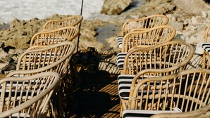 Wicker chairs arranged on a deck overlooking the ocean with palm trees and a rocky shoreline. - The Waves at Cane Bay (Kingshill)