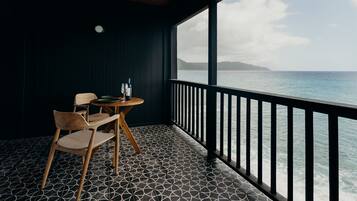 A balcony with a geometric patterned floor, a wooden table with chairs, and a view of the sea.