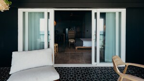A room with a bed, a chair, and a dining area visible through a sliding glass door. - The Waves at Cane Bay (Kingshill)