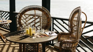 A round table with wicker chairs, a bottle of juice, and a menu on a terrace overlooking the sea.