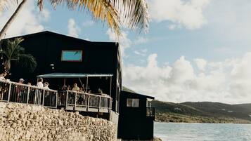 A coastal building with a balcony overlooking the sea, a stone wall, and a view of the landscape.