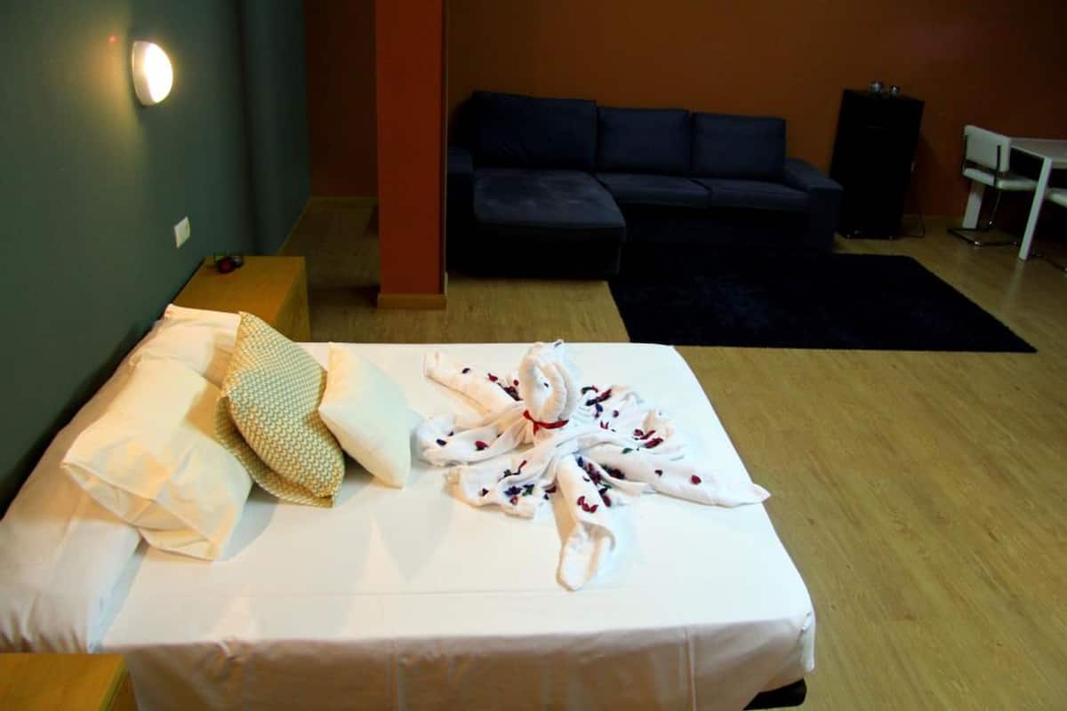 A hotel room with a bed, a sofa, a small table, and a speaker.