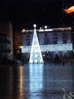 Un gran árbol de Navidad iluminado en una plaza abierta, con un edificio en el fondo.