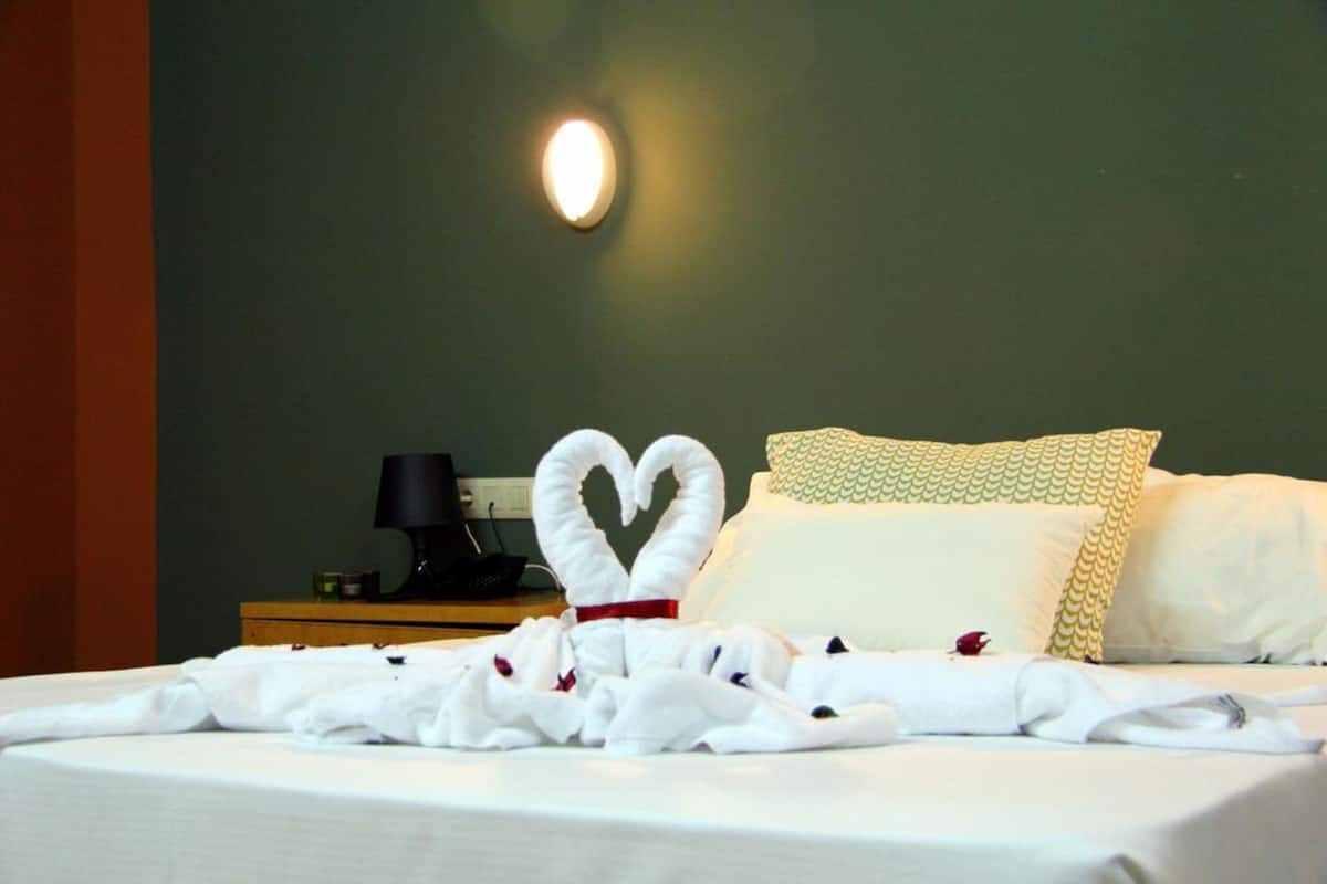 A neatly made bed with a heart-shaped towel arrangement and a pillow with a scalloped edge.