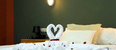 A neatly made bed with a heart-shaped towel arrangement and a pillow with a scalloped edge.