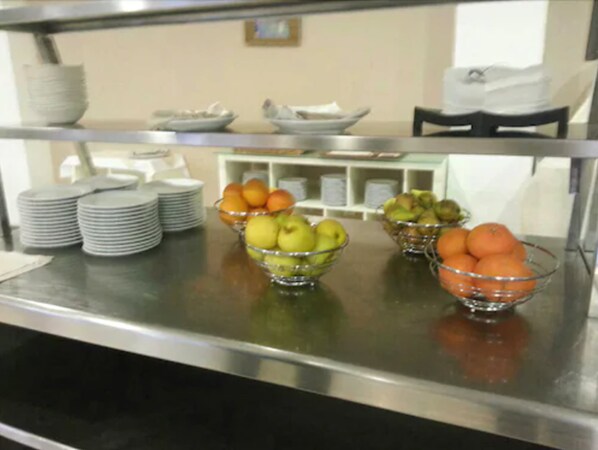 A buffet setup with bowls of fruit and stacked plates.