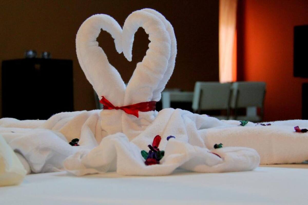 A bed with a towel arranged in the shape of a heart, tied with a red ribbon.