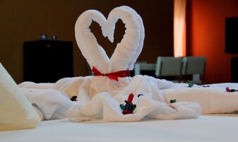 Una cama con una toalla dispuesta en forma de corazón, atada con un lazo rojo.